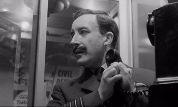 Movie still from “Dr. Strangelove or: How I Learned to Stop Worrying and Love the Bomb” (1964), directed by Stanley Kubrick – A man in a military uniform holding a gun; Close Up shot, Low angle