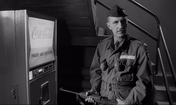 Movie still from “Dr. Strangelove or: How I Learned to Stop Worrying and Love the Bomb” (1964), directed by Stanley Kubrick – An old photo of a man holding a gun in front of a coke machine; Medium shot, Low angle