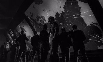 Movie still from “Dr. Strangelove or: How I Learned to Stop Worrying and Love the Bomb” (1964), directed by Stanley Kubrick – Black and white photograph of a group of people standing in front of a map of the world; Extreme Wide shot, Low angle