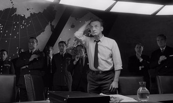 Movie still from “Dr. Strangelove or: How I Learned to Stop Worrying and Love the Bomb” (1964), directed by Stanley Kubrick – An old photo of a man in a suit and a tie; Medium shot, Low angle