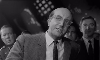 Movie still from “Dr. Strangelove or: How I Learned to Stop Worrying and Love the Bomb” (1964), directed by Stanley Kubrick – An old black and white photo of a man in a suit and tie; Close Up shot, Over the shoulder angle