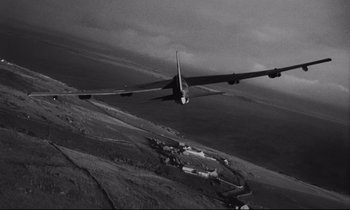 Movie still from “Dr. Strangelove or: How I Learned to Stop Worrying and Love the Bomb” (1964), directed by Stanley Kubrick – An airplane is flying over the ocean in a black and white photo; Extreme Wide shot, Overhead angle