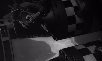 Movie still from “Dr. Strangelove or: How I Learned to Stop Worrying and Love the Bomb” (1964), directed by Stanley Kubrick – A man sitting on top of a checkerboard floor; Wide shot, Overhead angle