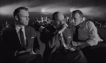 Movie still from “Dr. Strangelove or: How I Learned to Stop Worrying and Love the Bomb” (1964), directed by Stanley Kubrick – A group of men sitting next to each other holding drinks; Medium shot, Low angle