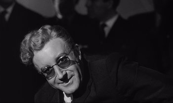 Movie still from “Dr. Strangelove or: How I Learned to Stop Worrying and Love the Bomb” (1964), directed by Stanley Kubrick – An older man wearing glasses and a suit; Close Up shot, Over the shoulder angle