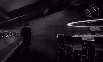 Movie still from “Dr. Strangelove or: How I Learned to Stop Worrying and Love the Bomb” (1964), directed by Stanley Kubrick – A man standing in front of a dining room table; Wide shot, Low angle