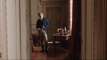 Movie still from “Emma.” (2020), directed by Autumn de Wilde – A man standing in front of a table in a room; Wide shot, Over the shoulder angle