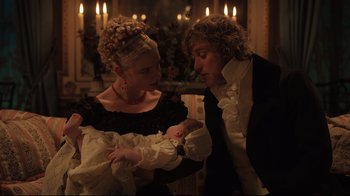 Movie still from “Emma.” (2020), directed by Autumn de Wilde – A man and a woman holding a baby in front of candles; Medium shot, High angle