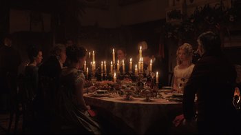 Movie still from “Emma.” (2020), directed by Autumn de Wilde – A group of people sitting around a dinner table with lit candles; Wide shot, High angle