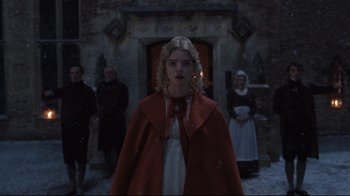 Movie still from “Emma.” (2020), directed by Autumn de Wilde – A woman in a red coat standing in front of a fire place; Medium shot, Low angle