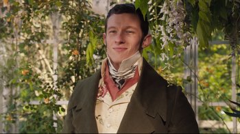 Movie still from “Emma.” (2020), directed by Autumn de Wilde – A man in a suit and a neck tie standing in front of a tree; Medium shot, Low angle