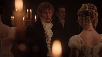 Movie still from “Emma.” (2020), directed by Autumn de Wilde – A man standing in front of candles in a dimly - lit room; Medium shot, Over the shoulder angle