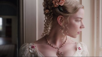 Movie still from “Emma.” (2020), directed by Autumn de Wilde – A young woman with blonde curly hair wearing a necklace and earrings; Close Up shot, Low angle
