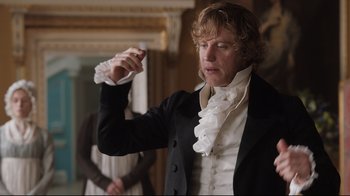 Movie still from “Emma.” (2020), directed by Autumn de Wilde – A man in a black and white suit holding a white object; Medium shot, Over the shoulder angle