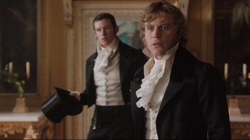 Movie still from “Emma.” (2020), directed by Autumn de Wilde – Two men dressed in period garb standing in front of a painting; Medium shot, Low angle