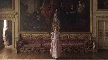 Movie still from “Emma.” (2020), directed by Autumn de Wilde – A woman in a pink dress standing in front of a painting; Wide shot, High angle