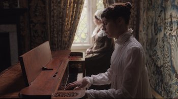 Movie still from “Emma.” (2020), directed by Autumn de Wilde – A young woman playing the piano in front of a window; Medium shot, Low angle
