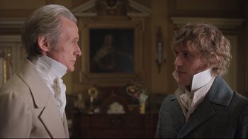 Movie still from “Emma.” (2020), directed by Autumn de Wilde – Two men standing next to each other in front of a painting; Close Up shot, Over the shoulder angle