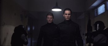 Movie still from “Equilibrium” (2002), directed by Kurt Wimmer – A couple of men standing next to each other in a room; Medium shot, Low angle