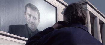 Movie still from “Equilibrium” (2002), directed by Kurt Wimmer – A man holding a gun in front of a picture of a man; Close Up shot, Over the shoulder angle