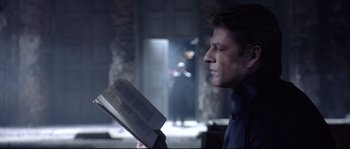 Movie still from “Equilibrium” (2002), directed by Kurt Wimmer – A man is reading a book in a dark room; Medium shot, Over the shoulder angle