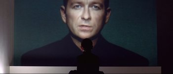 Movie still from “Equilibrium” (2002), directed by Kurt Wimmer – A person is sitting in front of a picture of a man; Close Up shot, Low angle