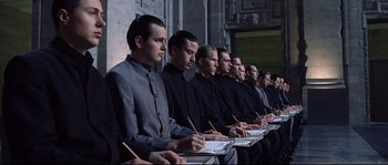 Movie still from “Equilibrium” (2002), directed by Kurt Wimmer – A group of men sitting next to each other in front of a wall; Medium shot, High angle