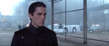 Movie still from “Equilibrium” (2002), directed by Kurt Wimmer – A man in a black jacket and a cop car in the background; Close Up shot, Over the shoulder angle