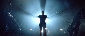 Movie still from “Equilibrium” (2002), directed by Kurt Wimmer – A man standing in the middle of a stage with lights; Wide shot, Low angle