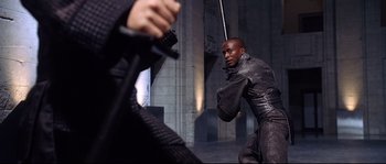 Movie still from “Equilibrium” (2002), directed by Kurt Wimmer – A man holding a sword in front of another man; Medium shot, Over the shoulder angle