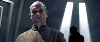 Movie still from “Equilibrium” (2002), directed by Kurt Wimmer – A bald man with a shaved head wearing a brown shirt; Close Up shot, Low angle