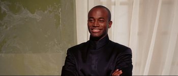 Movie still from “Equilibrium” (2002), directed by Kurt Wimmer – A man in a black jacket smiling for the camera; Close Up shot, Low angle