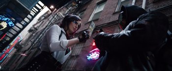 Movie still from “Free Guy” (2021), directed by Shawn Levy – A woman is holding a book in front of a neon sign; Medium shot, Over the shoulder angle