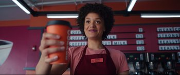 Movie still from “Free Guy” (2021), directed by Shawn Levy – A woman holding up a cup of coffee in a store; Close Up shot, Low angle