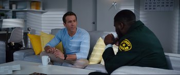 Movie still from “Free Guy” (2021), directed by Shawn Levy – Two men are sitting on a couch and talking to each other; Medium shot, Over the shoulder angle