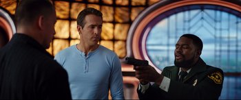 Movie still from “Free Guy” (2021), directed by Shawn Levy – A man holding a gun pointed at another man in front of a window; Medium shot, Over the shoulder angle