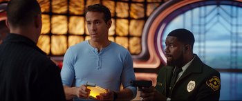 Movie still from “Free Guy” (2021), directed by Shawn Levy – A man and a woman holding guns in front of a wall; Medium shot, Over the shoulder angle