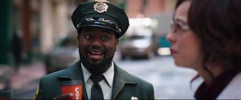 Movie still from “Free Guy” (2021), directed by Shawn Levy – A man in a uniform is smiling for the camera; Medium shot, Over the shoulder angle