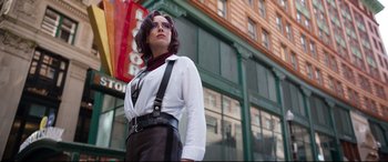 Movie still from “Free Guy” (2021), directed by Shawn Levy – A woman standing in front of a building wearing a white shirt and black pants; Medium shot, Low angle