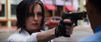 Movie still from “Free Guy” (2021), directed by Shawn Levy – A woman with glasses is holding a gun in her hand; Close Up shot, Over the shoulder angle