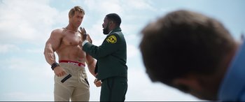 Movie still from “Free Guy” (2021), directed by Shawn Levy – A man in a green jacket is talking to another man in tan shorts; Medium shot, Over the shoulder angle