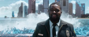 Movie still from “Free Guy” (2021), directed by Shawn Levy – A man wearing a suit and tie standing in front of a building; Medium shot, Over the shoulder angle