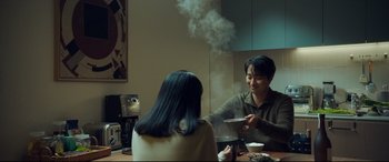 Movie still from “Decision to Leave” (2022), directed by Park Chan-wook – A man and a woman sitting at a dining table; Medium shot, Over the shoulder angle