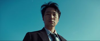 Movie still from “Decision to Leave” (2022), directed by Park Chan-wook – A person wearing a suit and tie; Close Up shot, Low angle