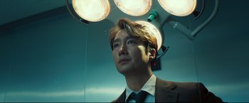 Movie still from “Decision to Leave” (2022), directed by Park Chan-wook – A man wearing a suit and tie standing under lights; Close Up shot, Low angle