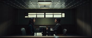Movie still from “Decision to Leave” (2022), directed by Park Chan-wook – A man and a woman sitting in front of each other at a desk; Wide shot, Low angle