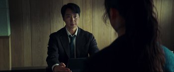 Movie still from “Decision to Leave” (2022), directed by Park Chan-wook – A man in a suit and tie talking to a woman in front of a wooden wall; Close Up shot, Over the shoulder angle
