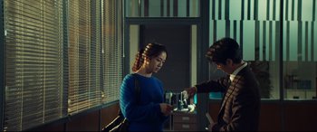 Movie still from “Decision to Leave” (2022), directed by Park Chan-wook – A woman in a blue sweater is looking at a cell phone; Medium shot, Low angle
