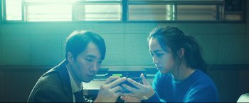 Movie still from “Decision to Leave” (2022), directed by Park Chan-wook – A man and a woman looking at a cell phone; Medium shot, High angle