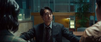 Movie still from “Decision to Leave” (2022), directed by Park Chan-wook – A man wearing a suit and tie sitting in a chair; Medium shot, Low angle